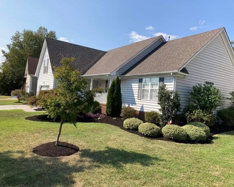 Landscaper maintenance in a garden bed full of evergreen shrubs and annual flowers.