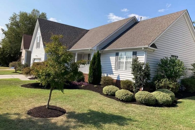 Landscaper maintenance in a garden bed full of evergreen shrubs and annual flowers.